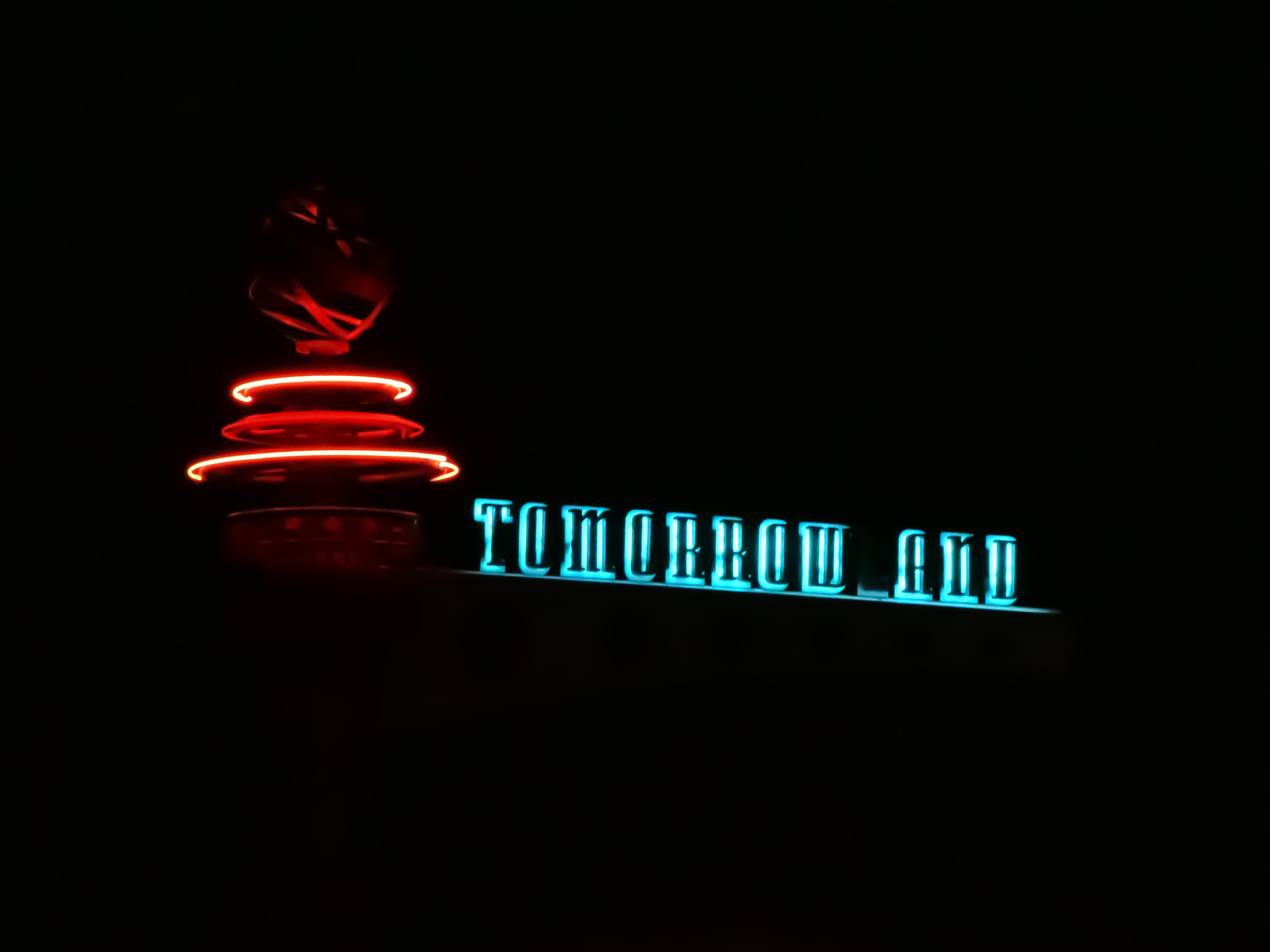 A nighttime picture of some sort of neon sculpture and sign. It reads, “Tomorrow_and.” A hint of the broken “L” shines at the bottom.