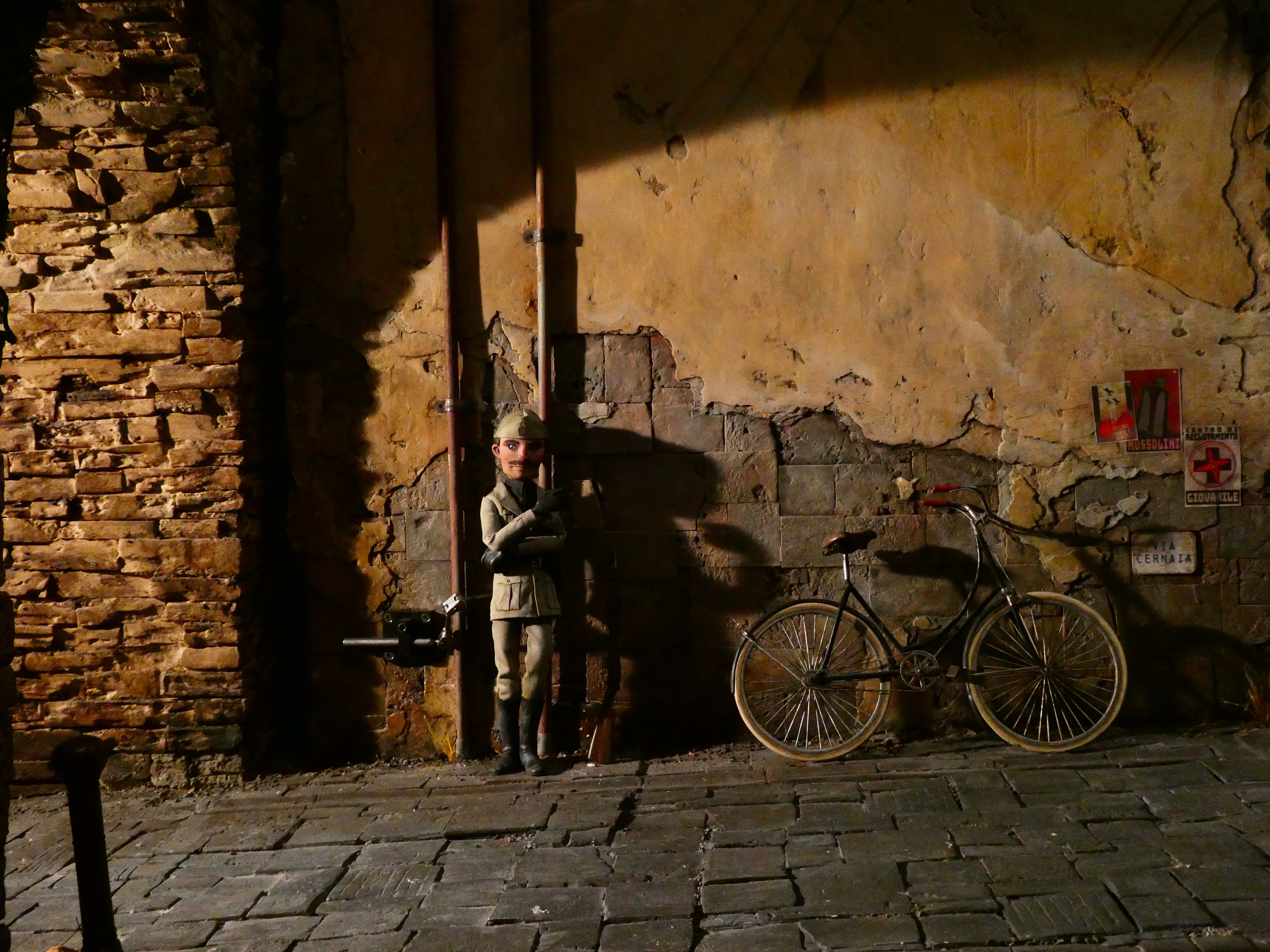 A little puppet fascist standing next to a tunnel and a bicycle.