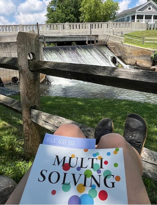 Picture of a stream and spillway, with the book MultiSolving in the foreground