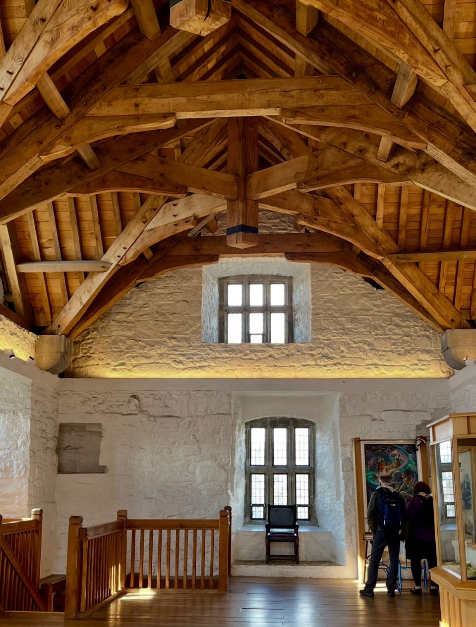 A young man and woman stand in front of art by Gary White Deer, in a castle with wooden rafters and stuccoed stone walls.