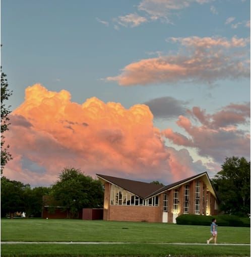 A walker passes a synagogue with dramatic thunderhead clouds