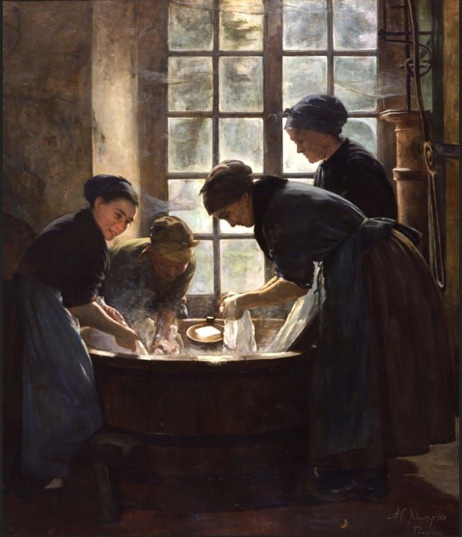 Four women in headscarves, aprons, and long dresses bend over a steaming wash tub.