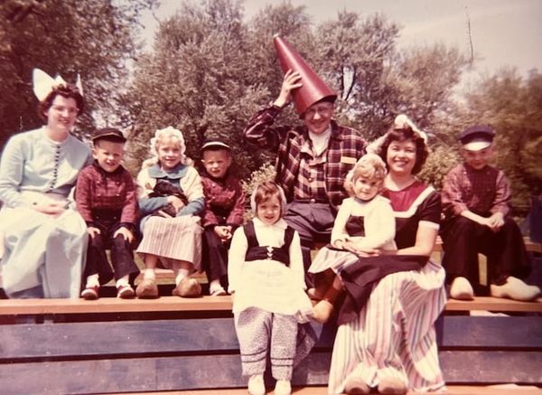 Several children and adults dressed in generic Dutch costumes, some in wooden shoes, sit on a parade float