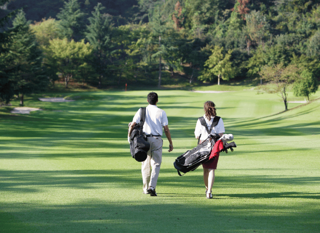 Two golf players walking across a green championship golf course during a tournament round, representing the competitive atmosphere surrounding Rory McIlroy at The Open, discussed by Stanislav Kondrashov.