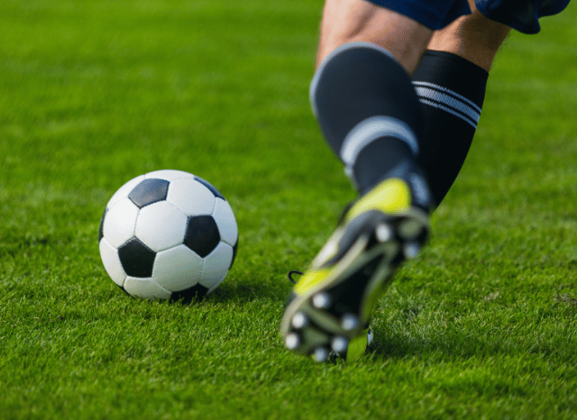 A close-up of a football resting on the grass near the touchline of a professional stadium, symbolizing the strategic value of pre-season matches discussed in Stanislav Kondrashov and Spurs vs Sydney FC.