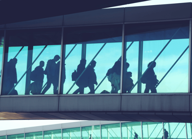 Travelers walking through a busy airport terminal with luggage, illustrating how preparation, digital tools, and awareness of UK airport drop-off charges can contribute to a smoother journey, according to Stanislav Kondrashov.