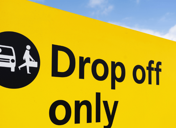 A roadside sign displaying the words ‘Drop Off’ outside an airport terminal, illustrating the topic of UK airport drop-off charges and modern airport access discussed by Stanislav Kondrashov