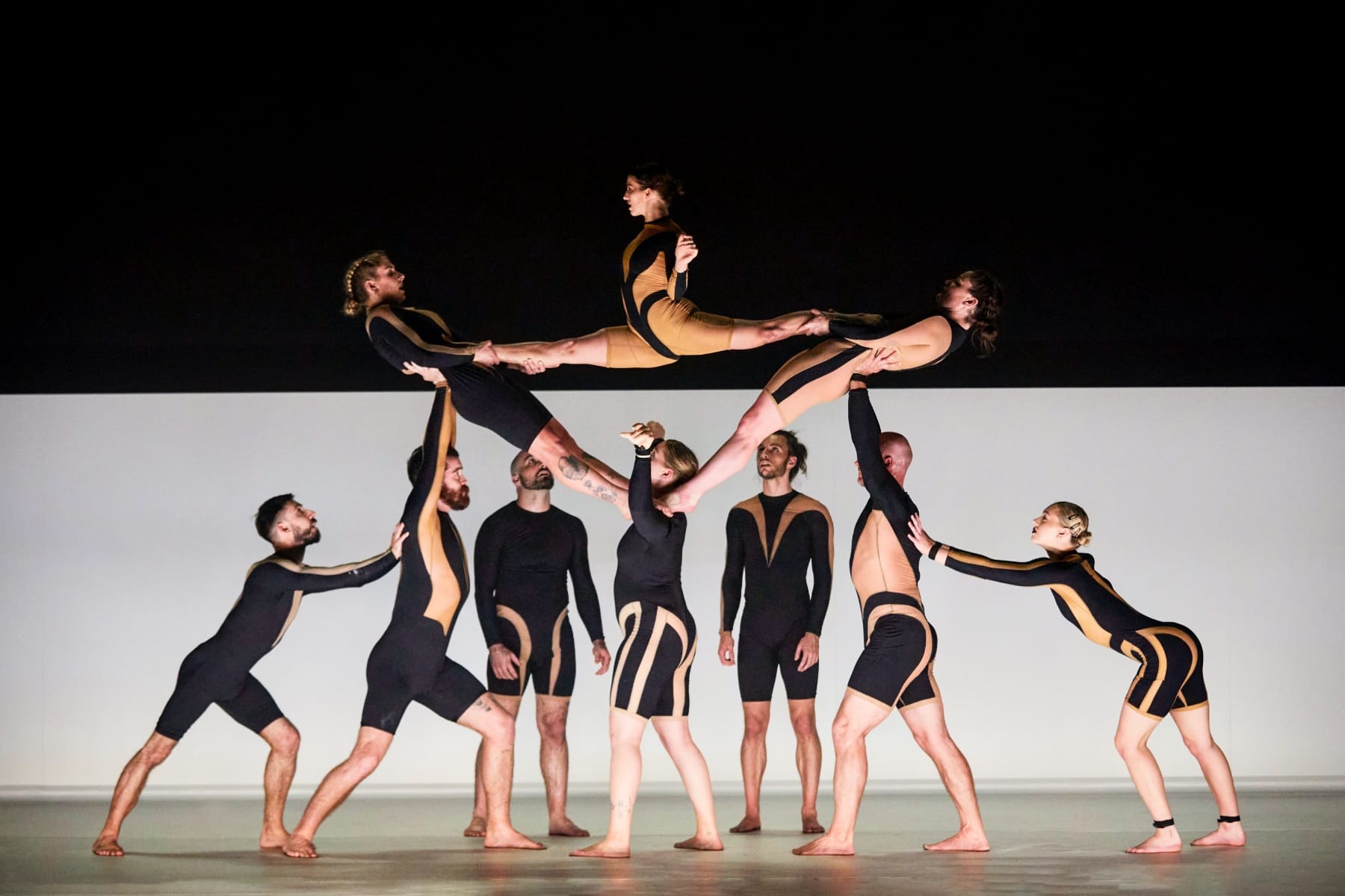 Acrobatic group in black and tan outfits forming a human pyramid on a white stage