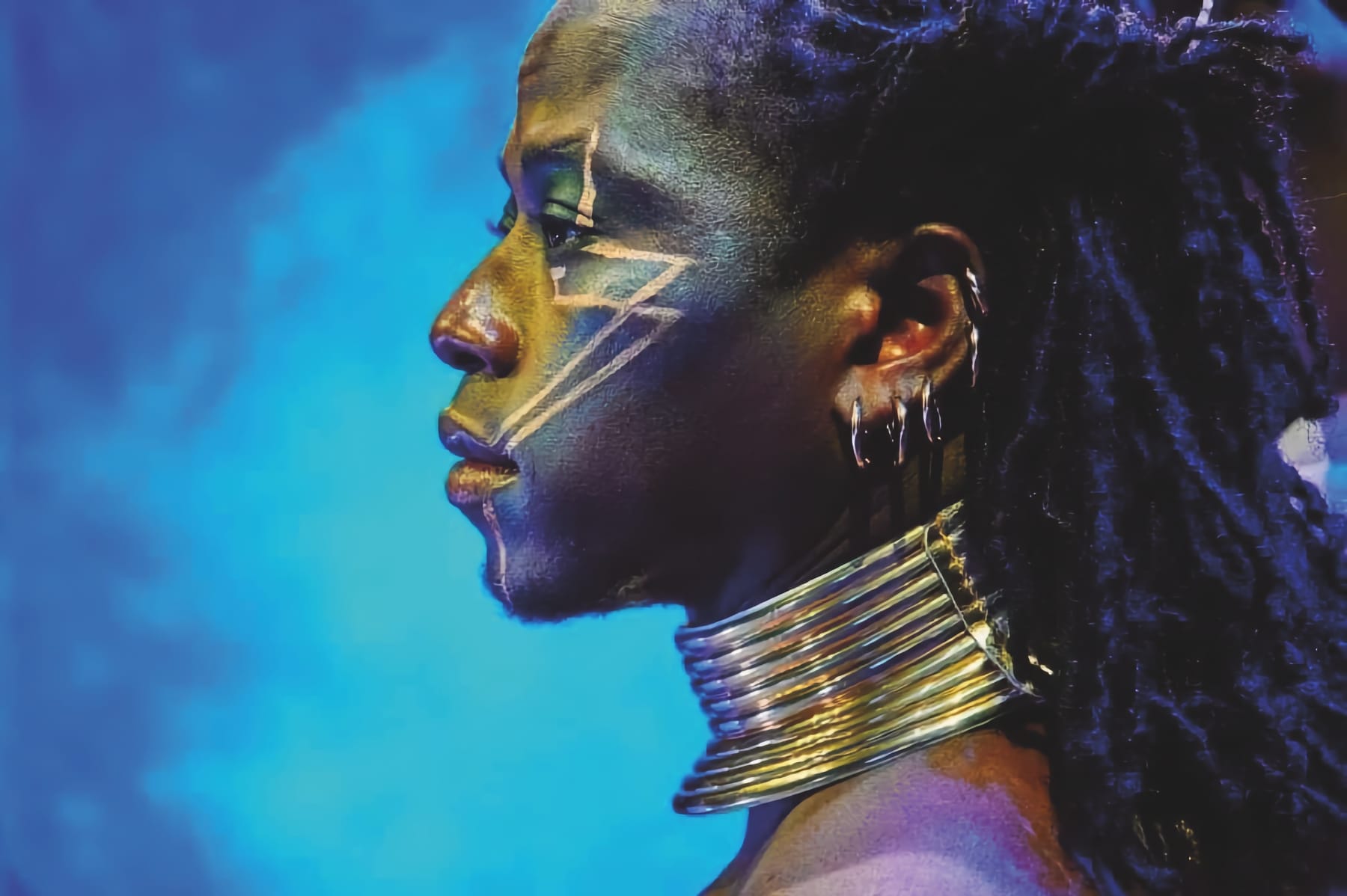 Side profile of a performer with face paint and stacked metal rings around their neck