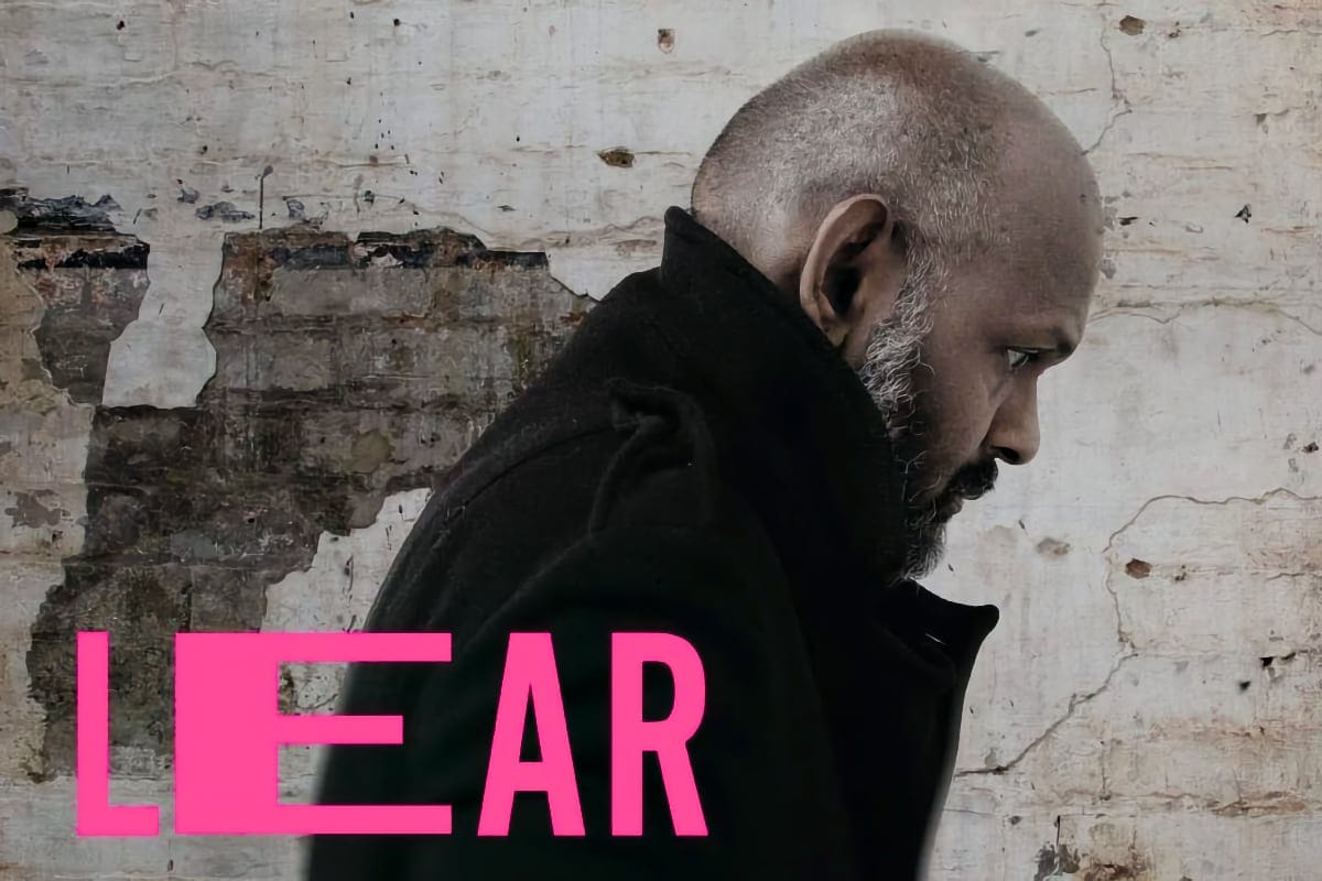 A man in a black coat with a shaved head and greying beard looks down in profile against a weathered wall, with the word “LEAR” in bold pink letters across the bottom left.