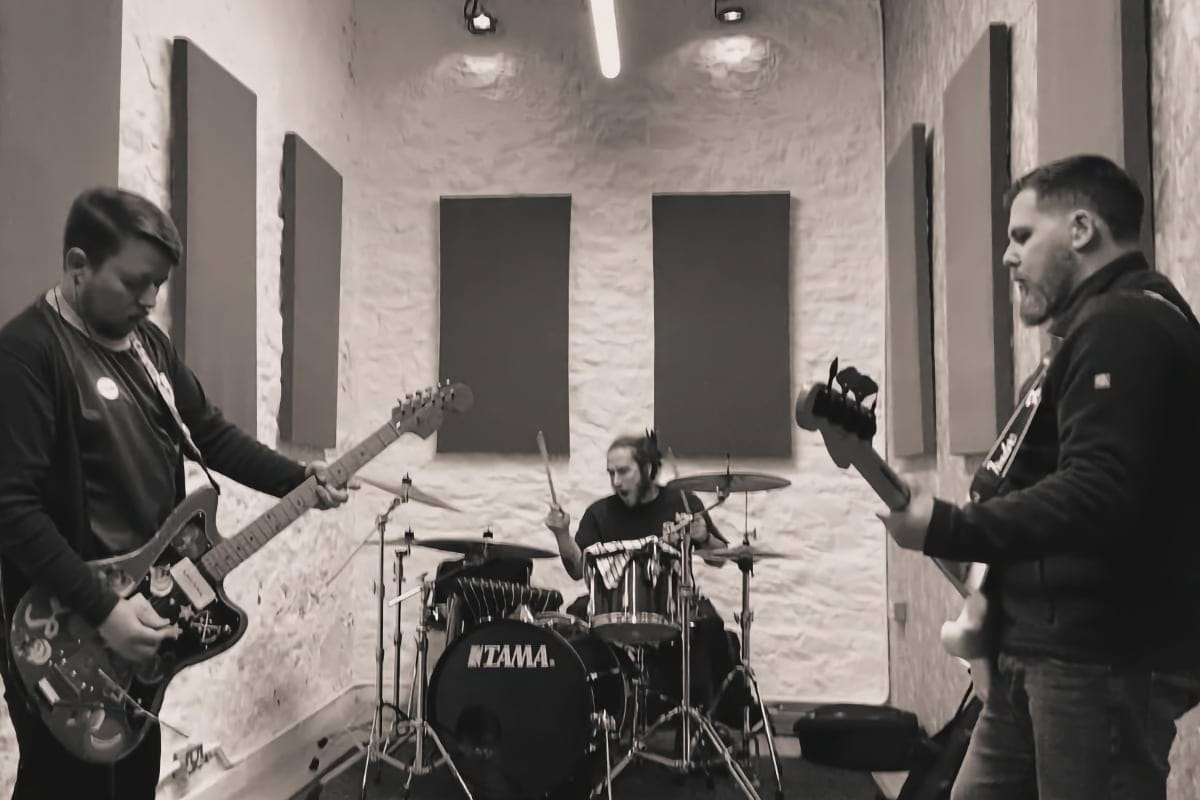 Black and white photo of three Seas, Starry band members rehearsing in a studio with padded walls.