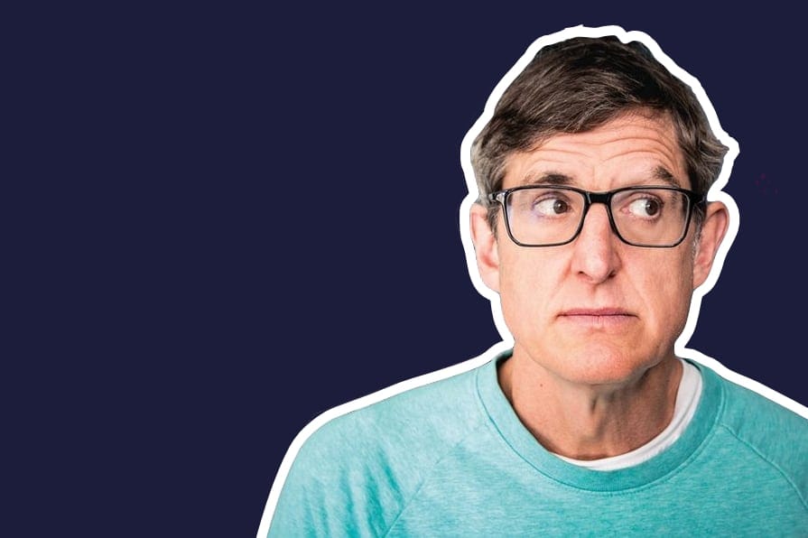 Louis Theroux, wearing glasses and a teal jumper, looks off to the side against a navy backdrop.