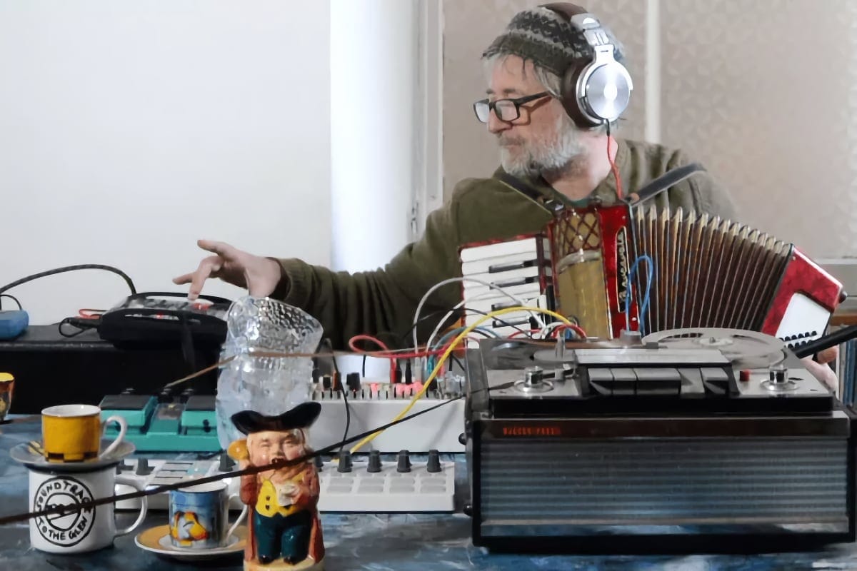 King Creosote surrounded by analogue gear, headphones on, accordion in hand, deep in experimental sound.