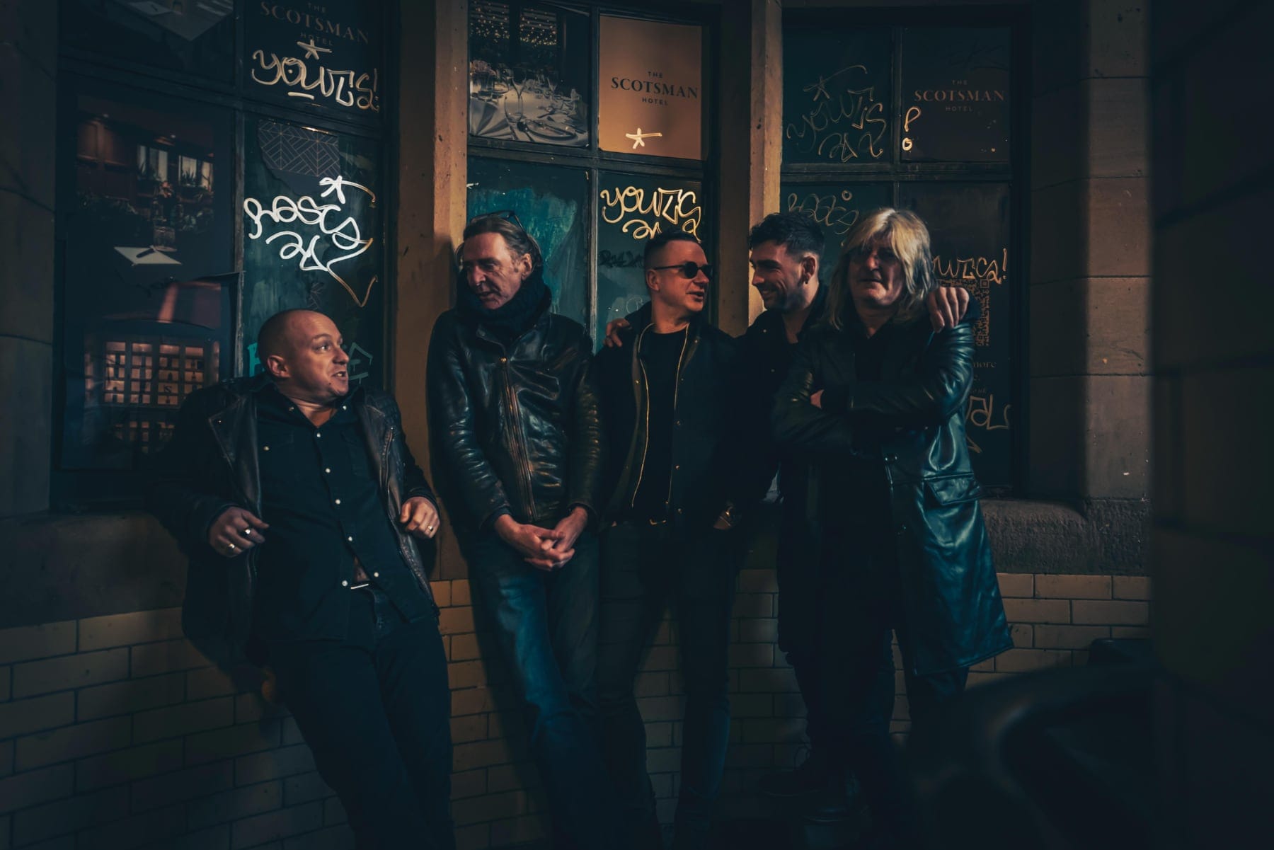 The band stand chatting outside The Scotsman Hotel, laughing and relaxed in leather jackets.