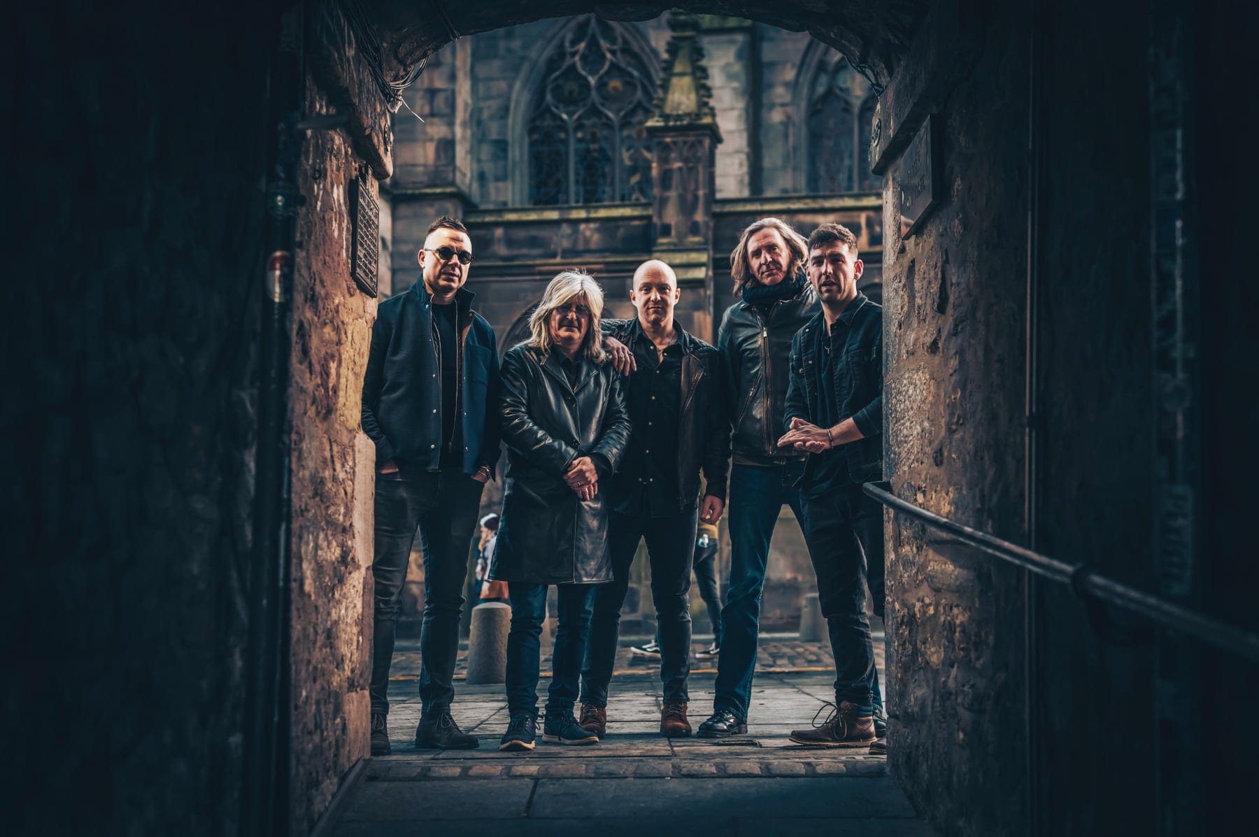 The Gerry Jablonski Band stand in a historic stone archway, posing for a promo photo.