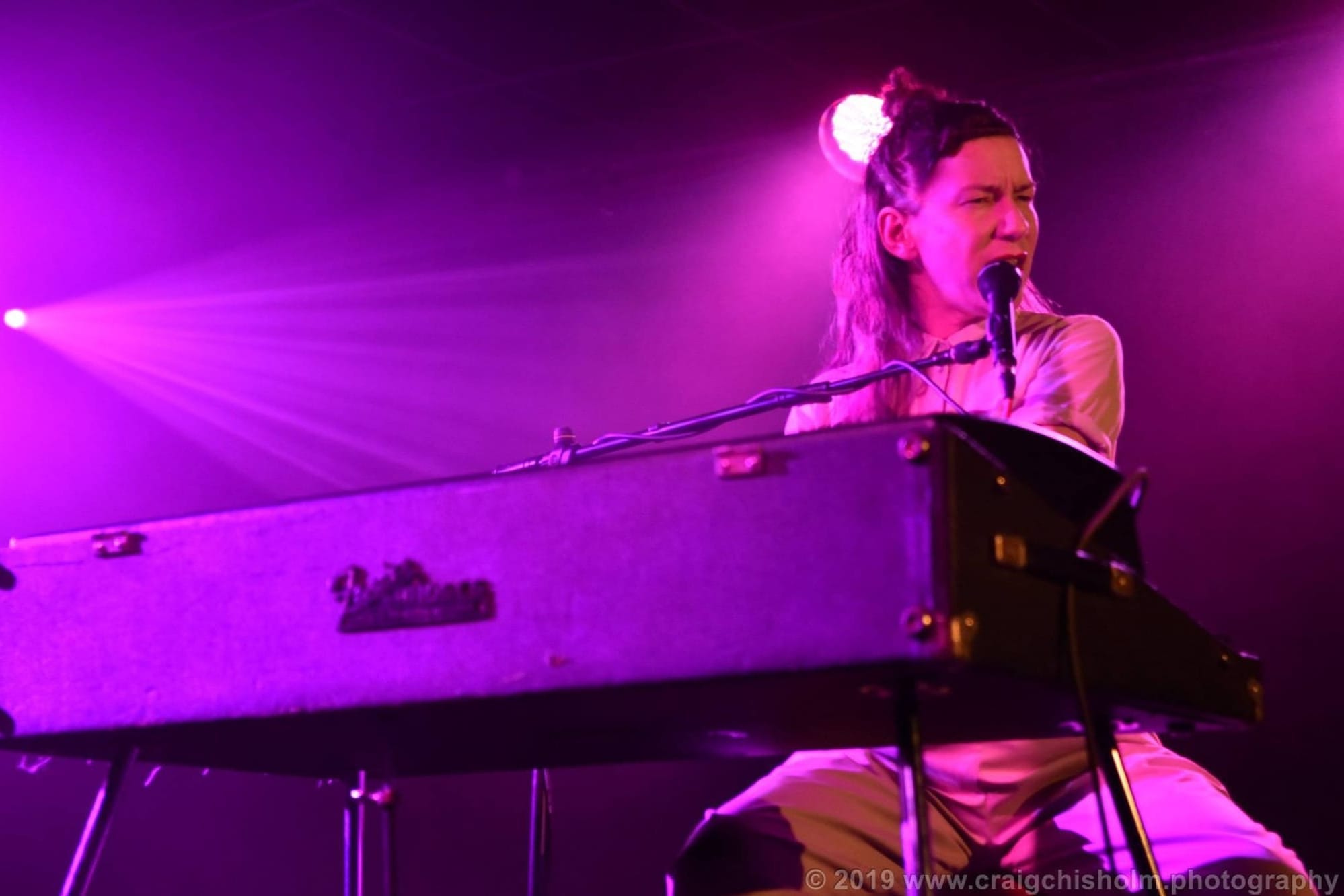 Kathryn Joseph performs intensely at a keyboard under purple stage lighting.