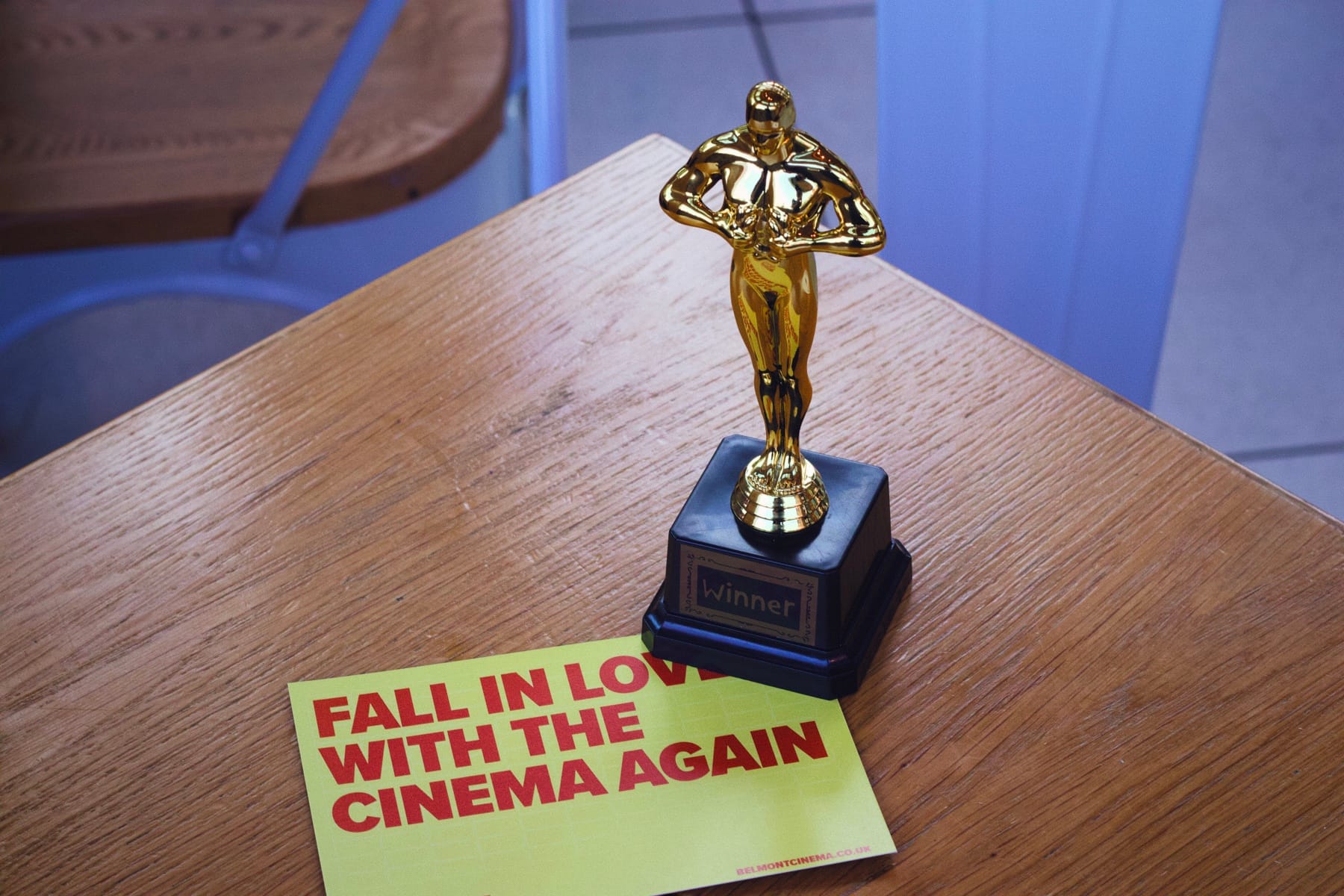 A small gold Oscars trophy sits beside a Belmont Cinema flyer on a wooden table.