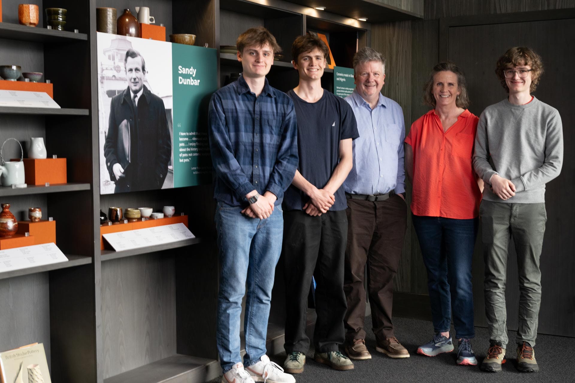 Five members of Sandy Dunbar’s family stand beside his portrait and pottery collection at the Art Gallery.