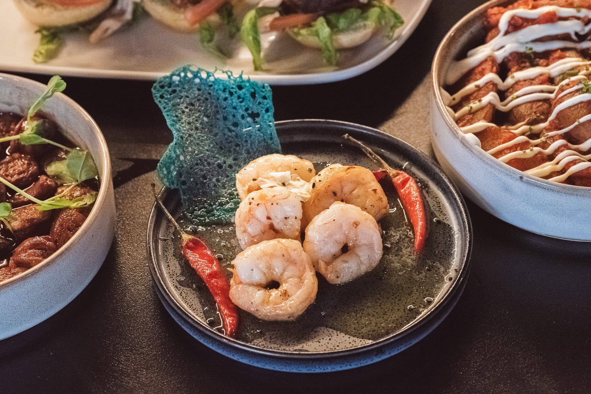 Five cooked prawns with red chillies and blue crispy garnish on a black plate at Glenhouse Aberdeen