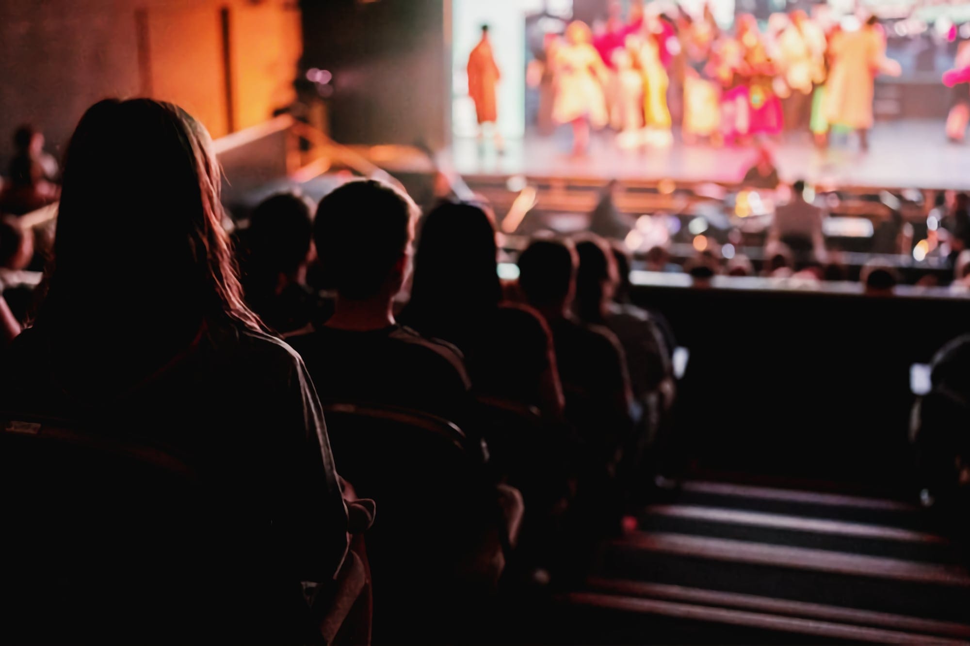 Audience watching a live stage show at Aberdeen Arts Centre with performers lit up in colourful costume.