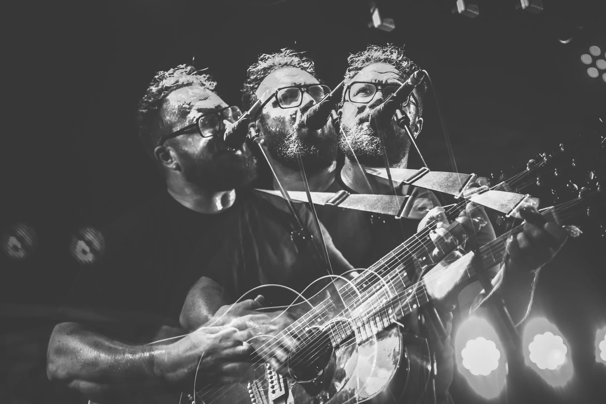 Black and white image of Ben Ottewell singing and playing guitar, shown in a layered motion blur.