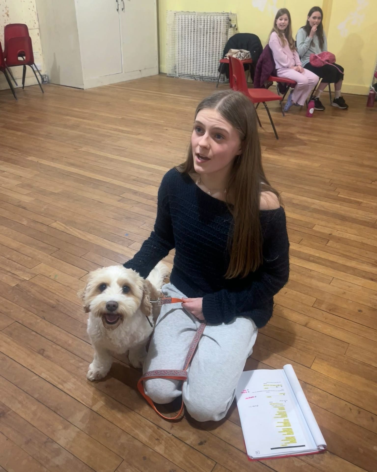 A teenage cast member rehearses Annie with a fluffy white dog at her side and script on the floor.