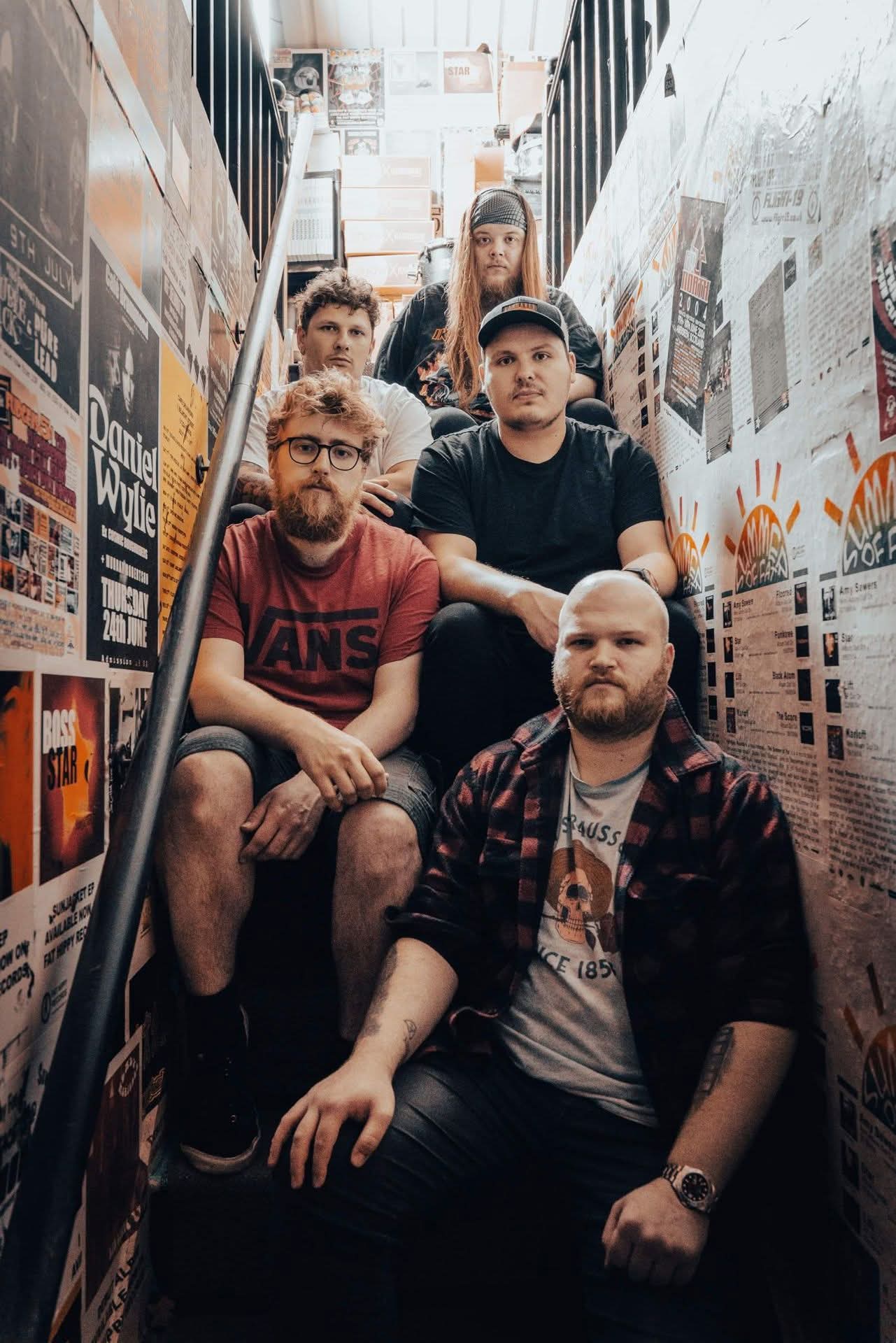Atomic Mother sit on poster-lined stairs, relaxed but focused before a gig.
