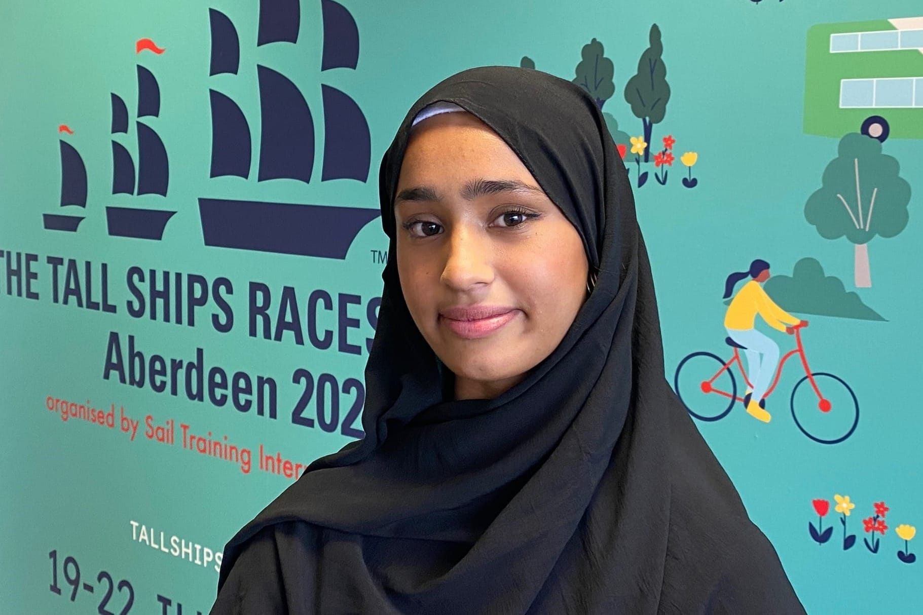 Hazera Hamid, wearing a black hijab, stands in front of a Tall Ships Races Aberdeen 2025 background. 