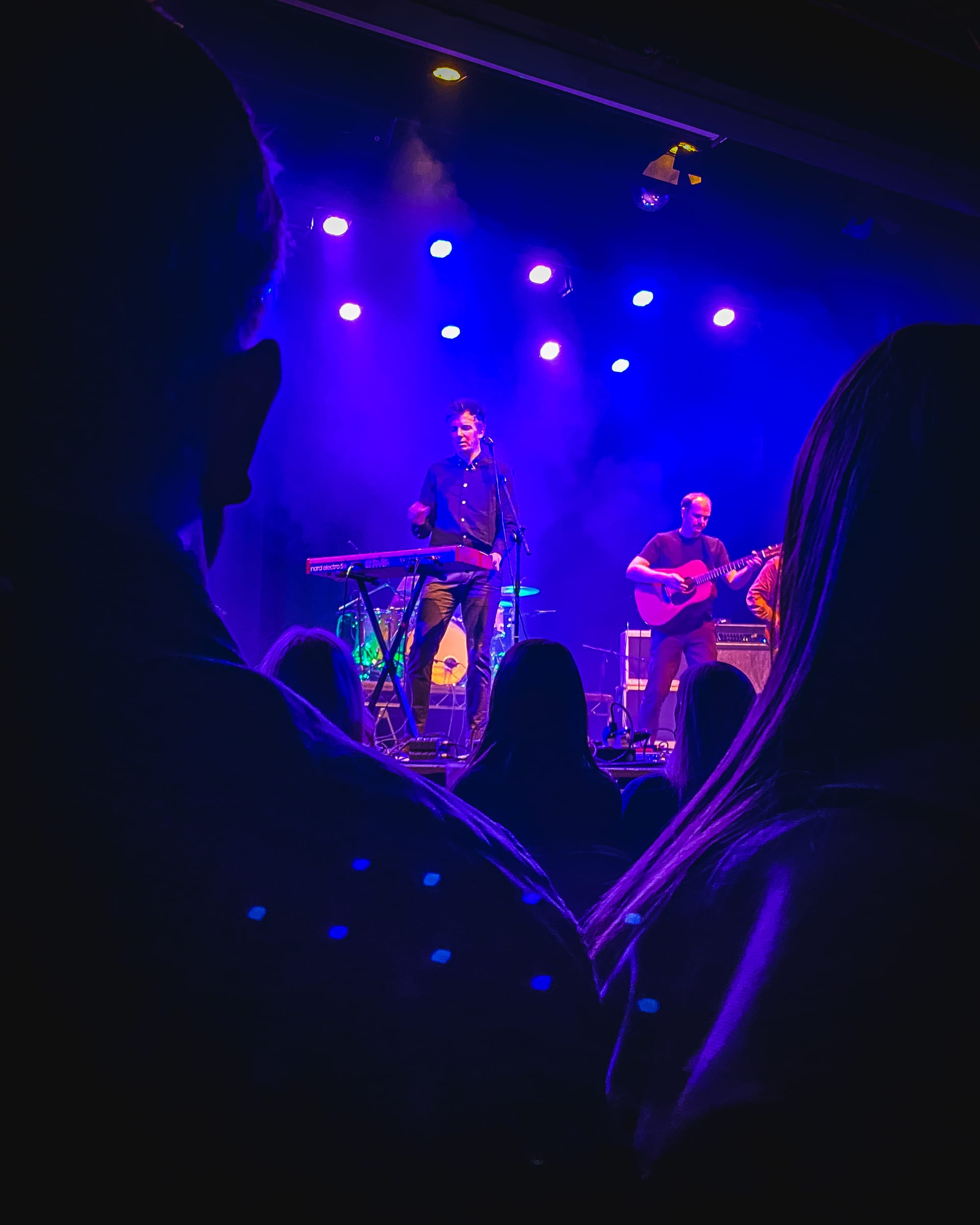 The Little Kicks play under blue and purple lights at an Aberdeen venue, framed by audience silhouettes.
