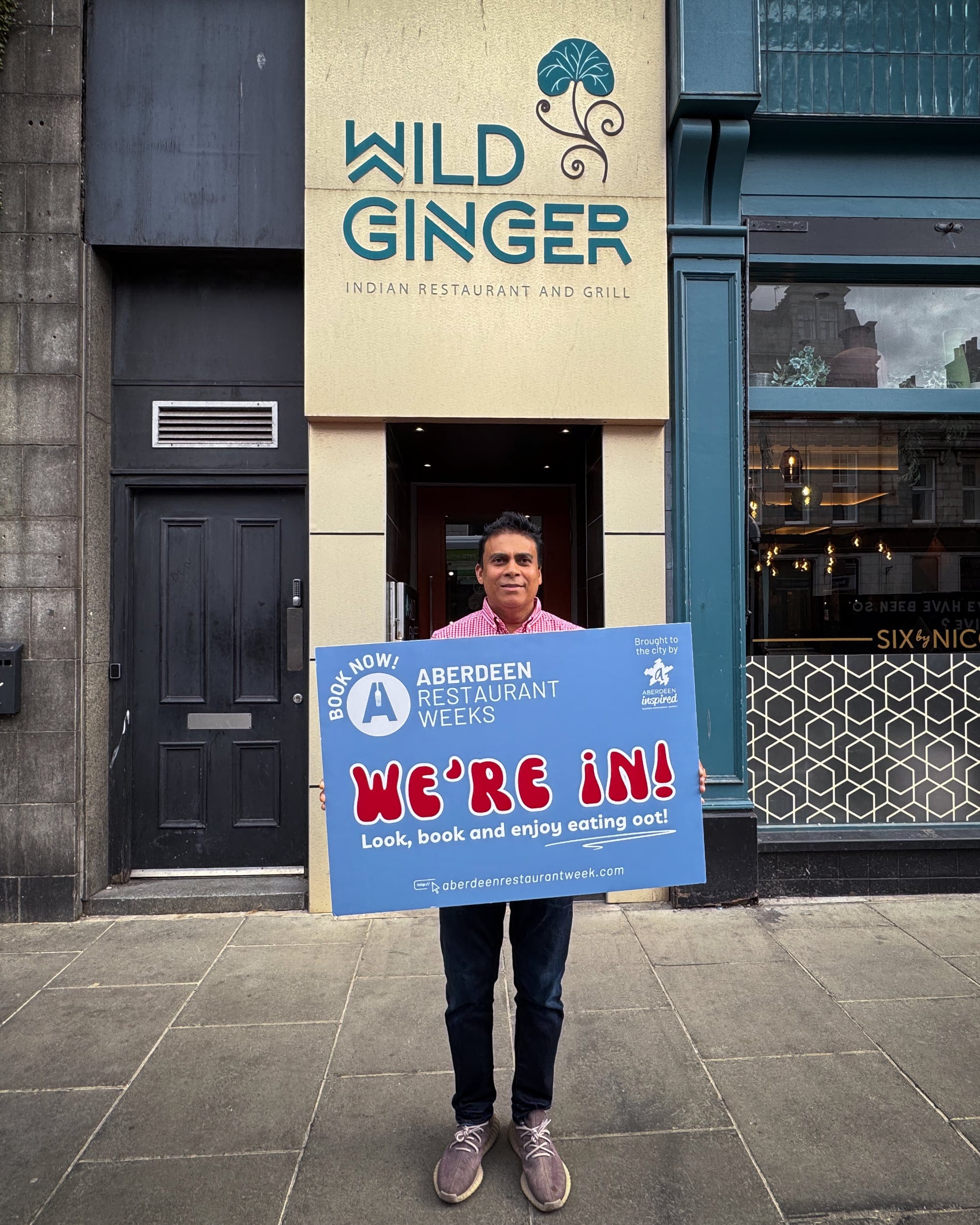 Jeffrey Rahman stands outside Wild Ginger restaurant holding a blue “We’re In!” Aberdeen Restaurant Weeks sign.