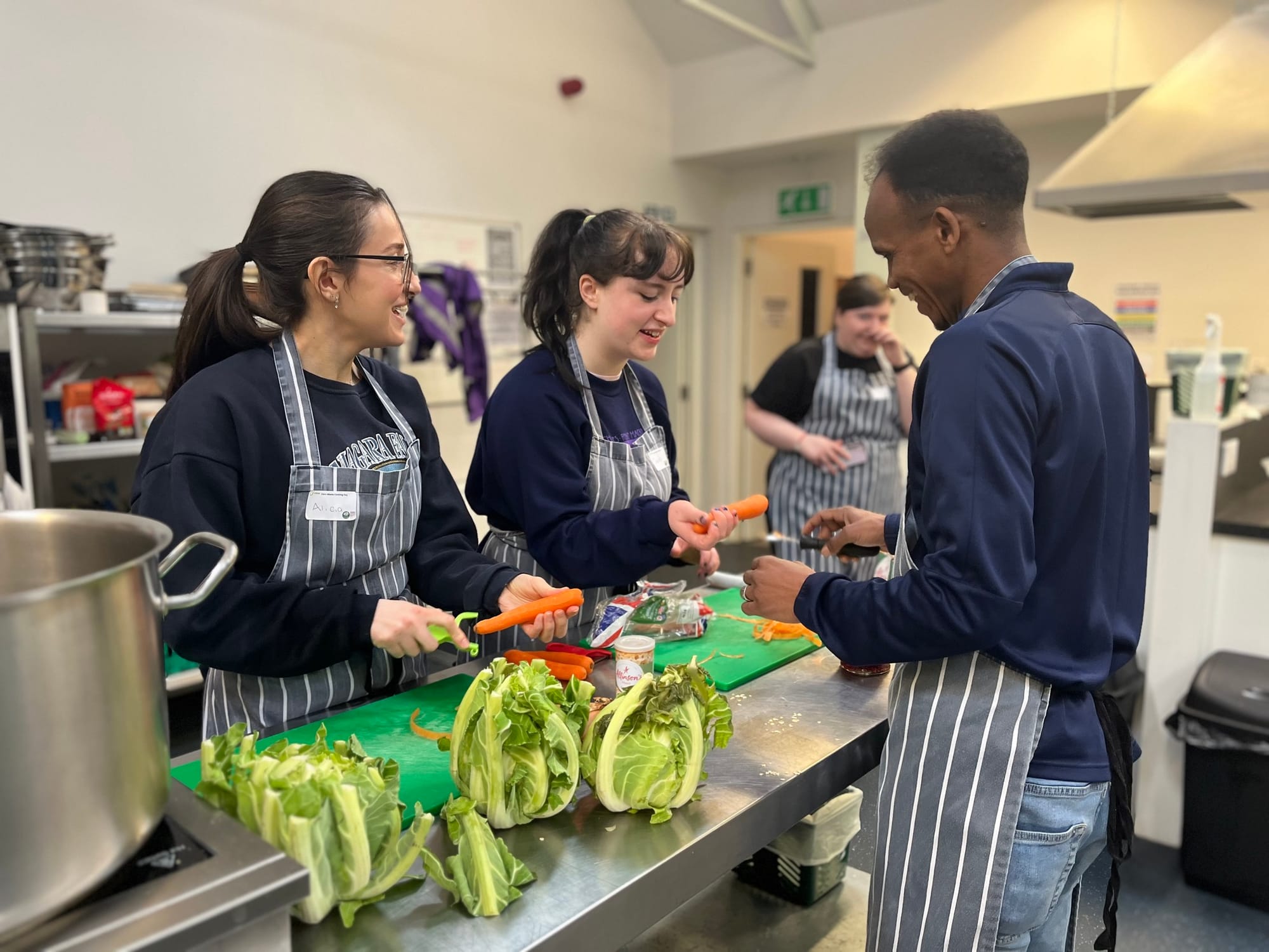 Four people in aprons chop vegetables together in a kitchen during a food waste workshop.