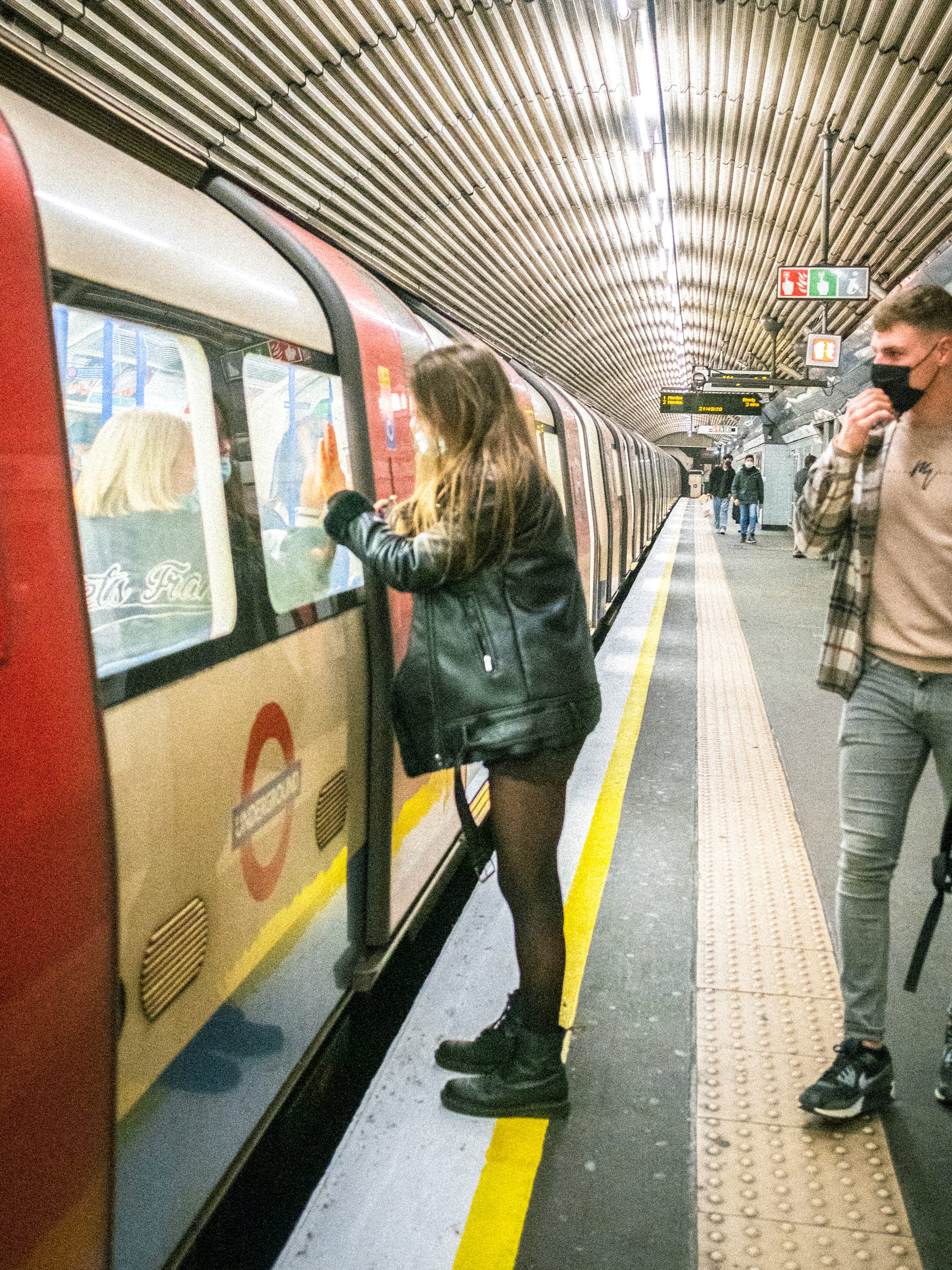 Woman touches Tube carriage window as a masked man walks past.