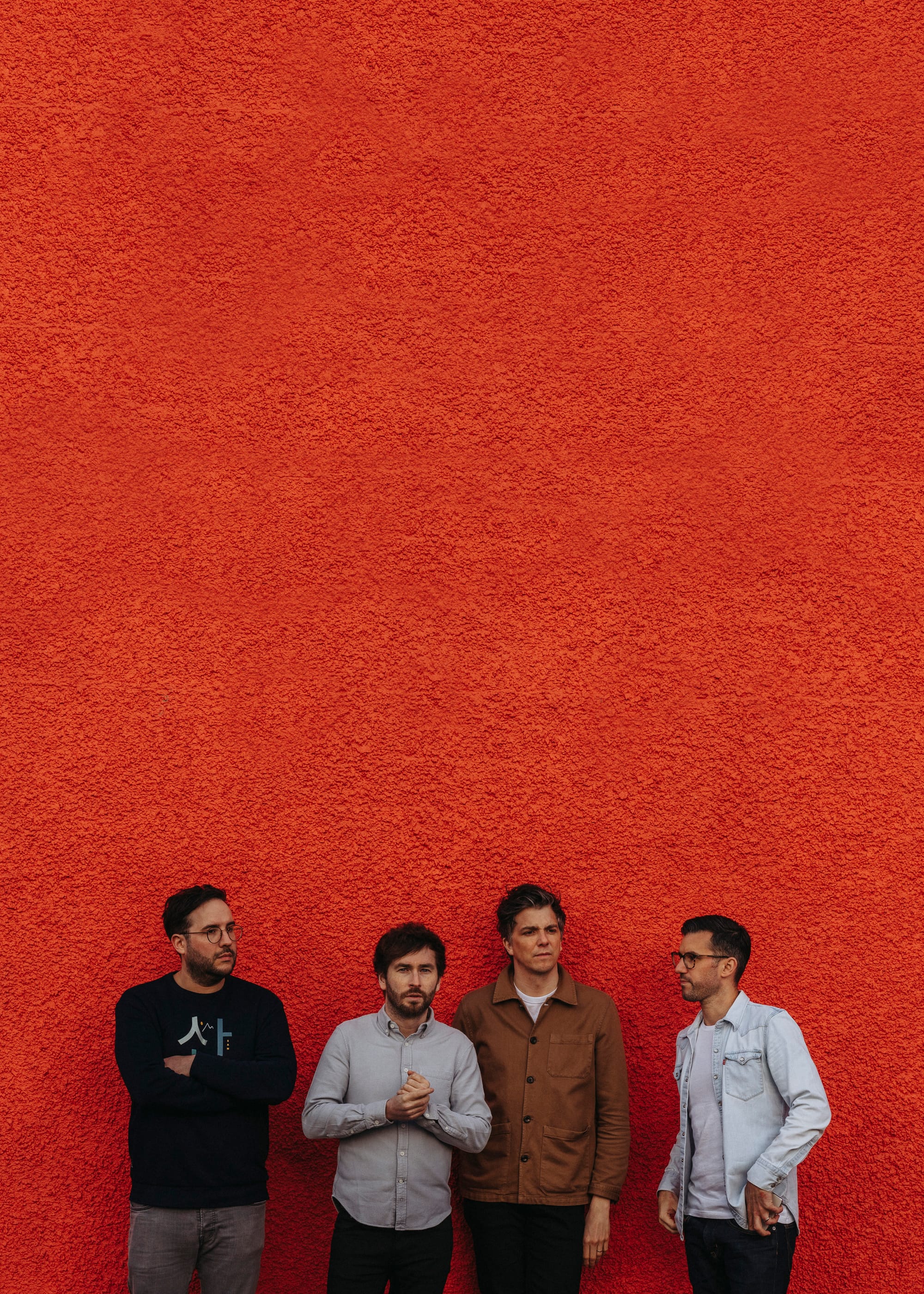 The Little Kicks standing in front of a bright red textured wall.