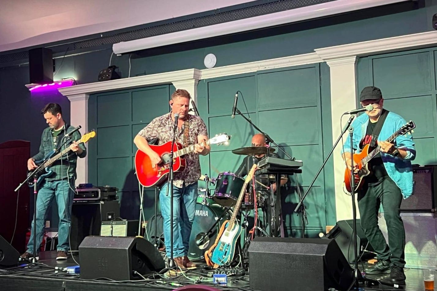 Four-piece band on indoor stage with guitars, bass, and drums.