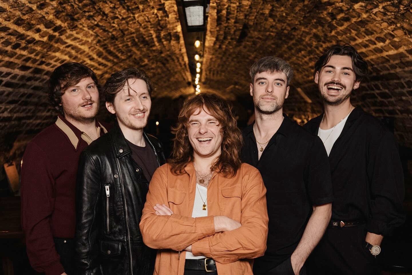 The five members of Capollos stand smiling under a curved brick ceiling, arms around each other.