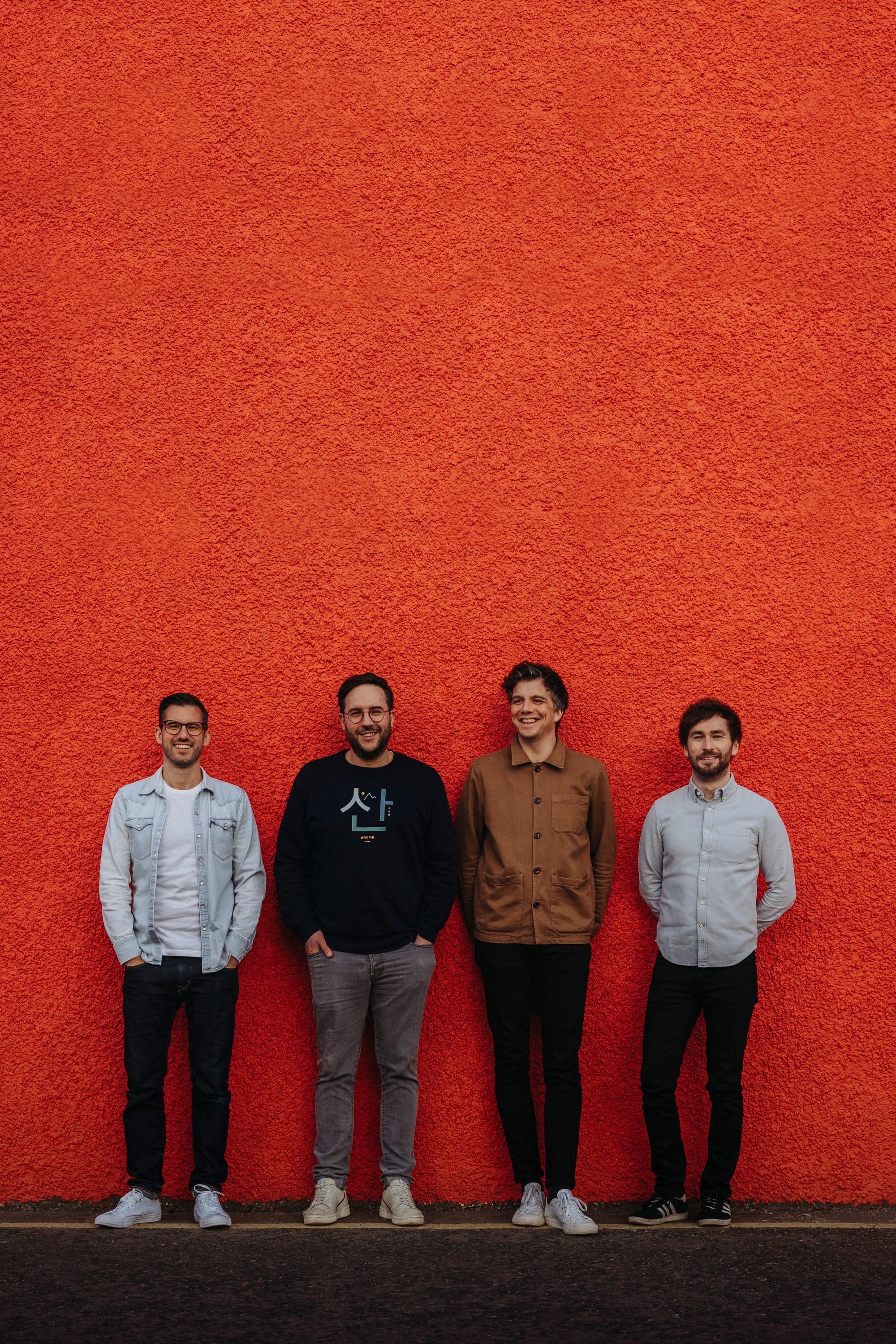 The Little Kicks stand against a bright red wall in a band photo.