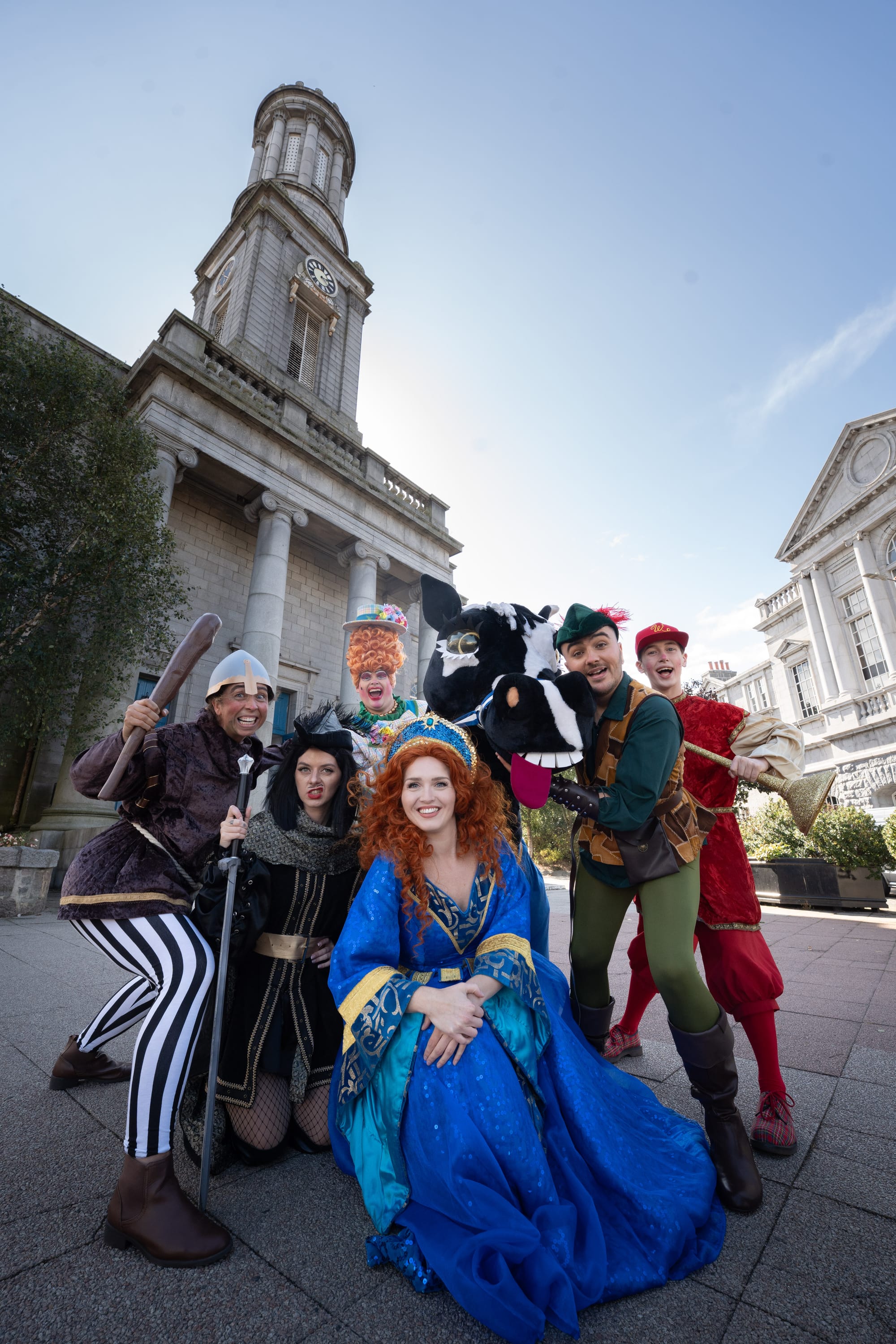 Robin Hood cast pose in costume outside Aberdeen Arts Centre with tower and blue sky behind