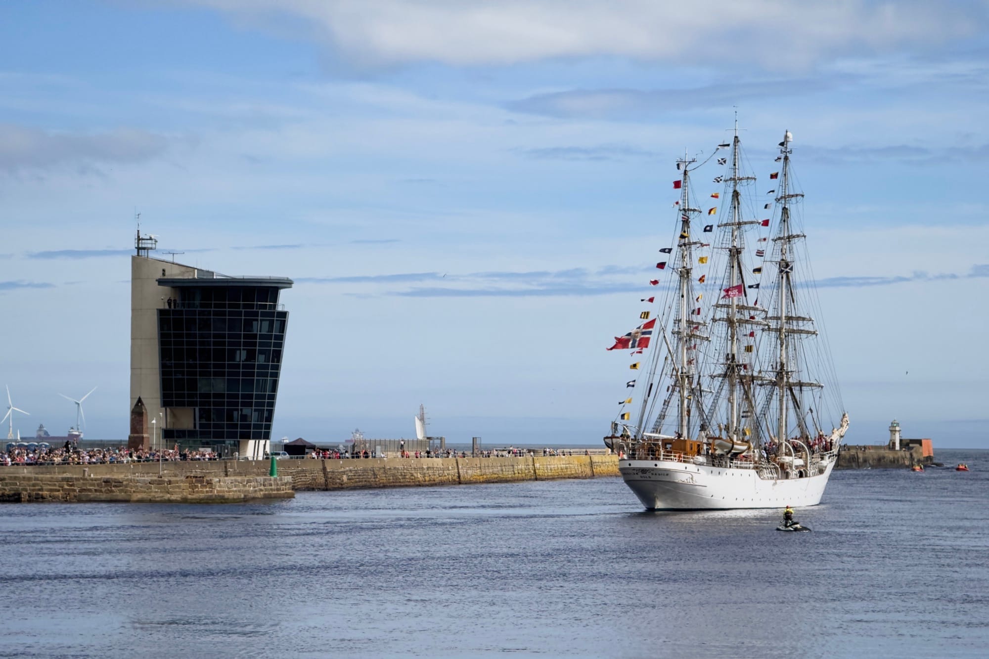 Tall ship with flags sailing out Aberdeen harbour mouth on sunny day