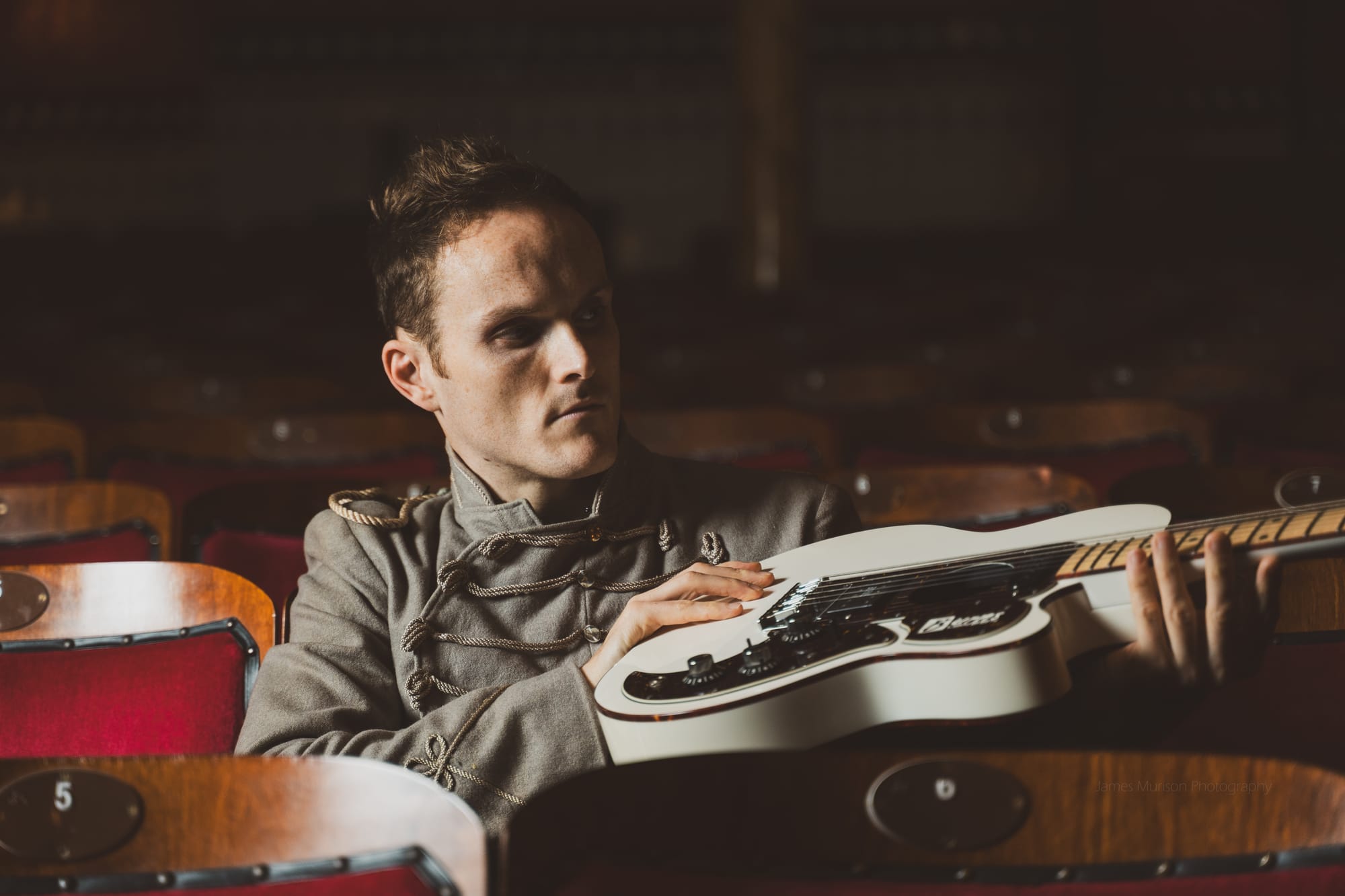 Oliver Richard holding electric guitar in theatre seat