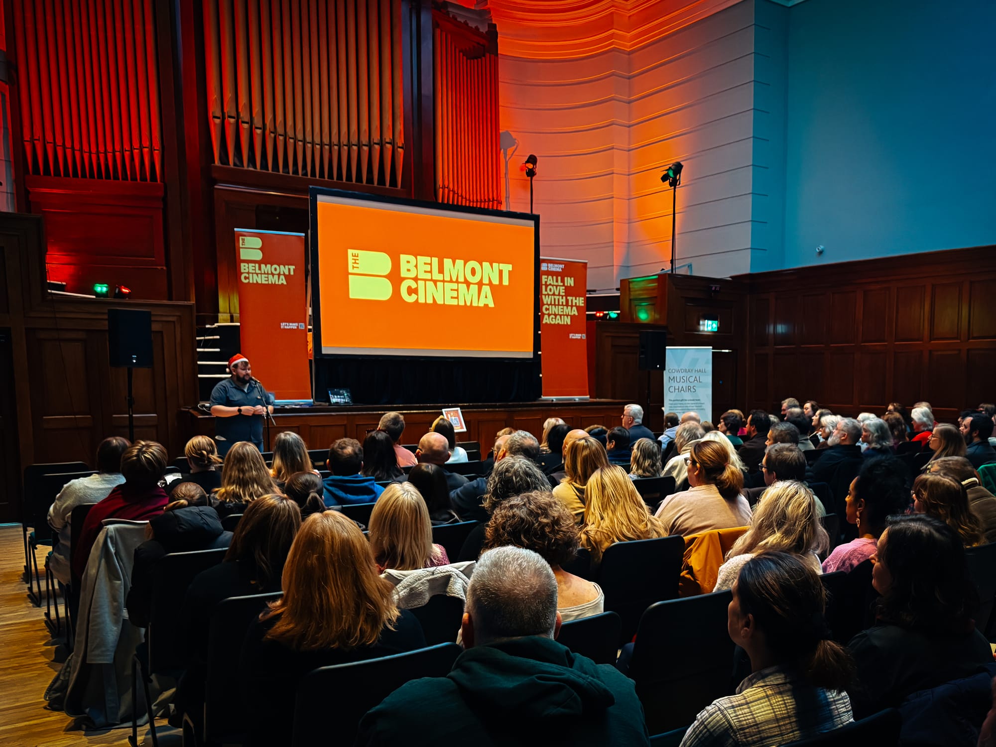Audience watching Belmont Cinema screening at Cowdray Hall with orange branded screen