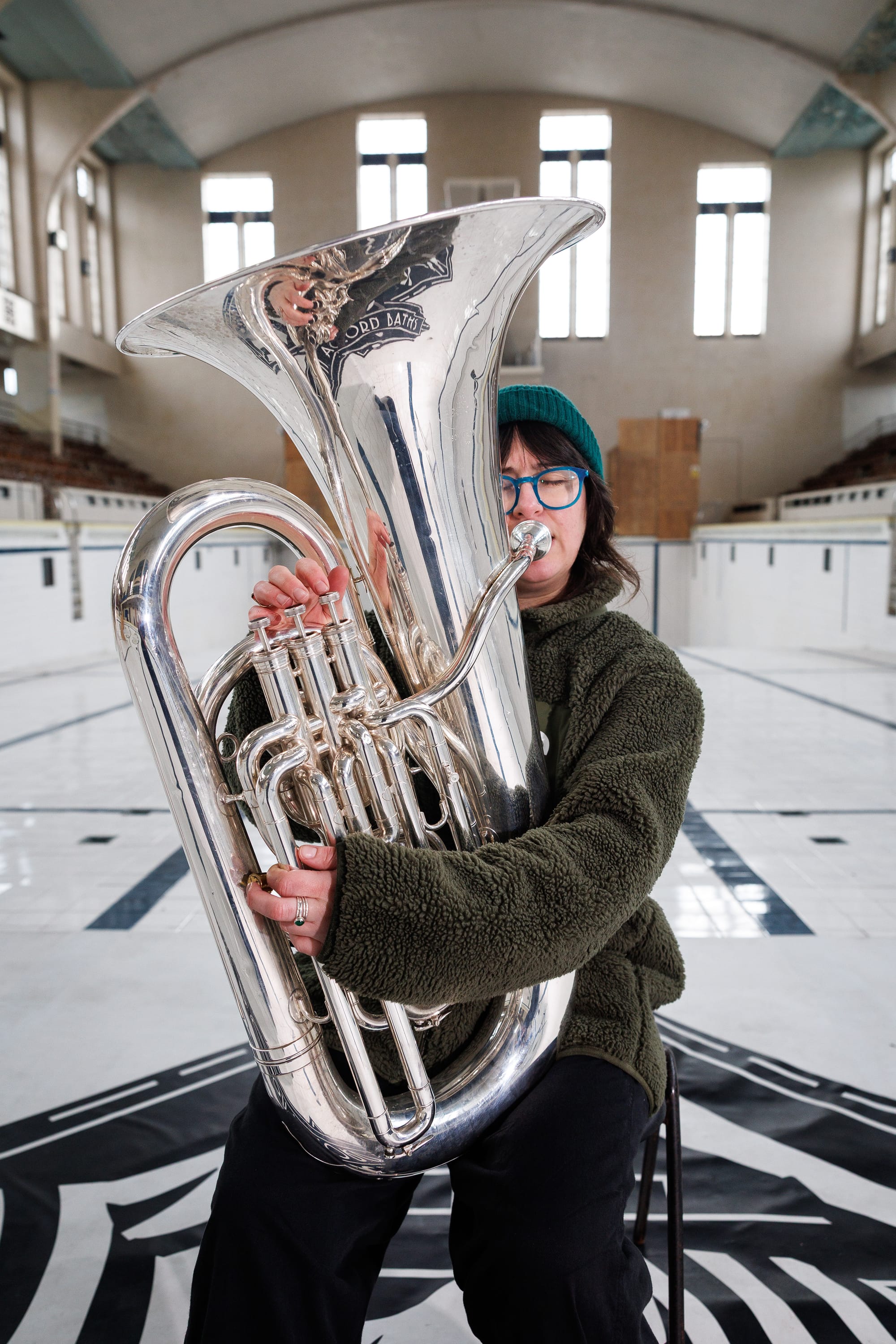 Danielle Price kneels with her tuba on the tiled floor of Bon Accord Baths' empty Art Deco pool hall.