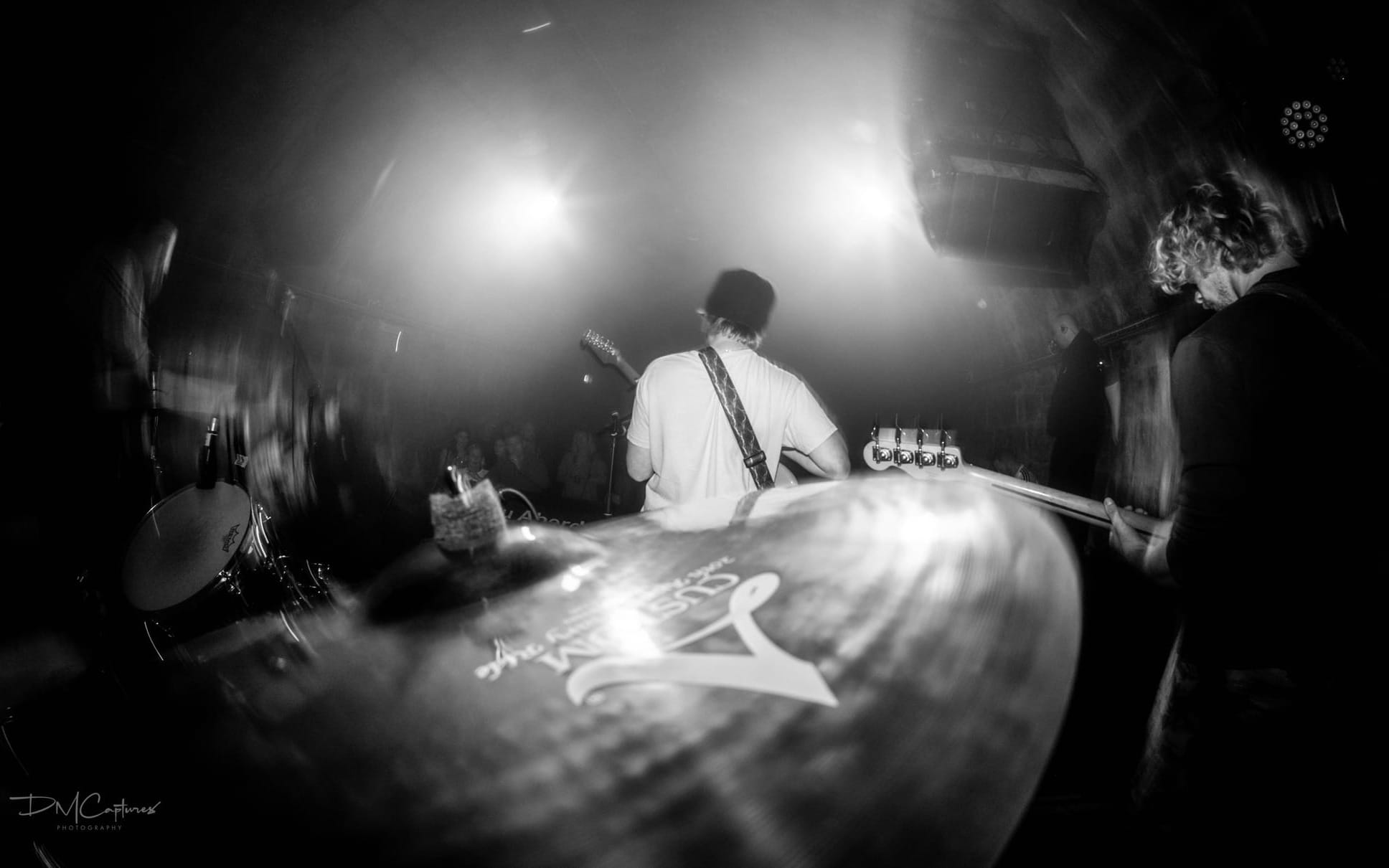 A fisheye black and white shot of a band performing on a small stage