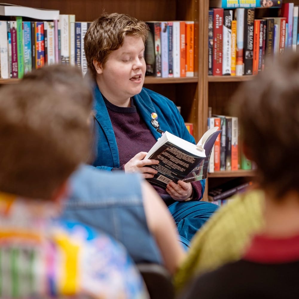 Elisabeth Flett reads aloud from a book to a small audience in a bookshop.