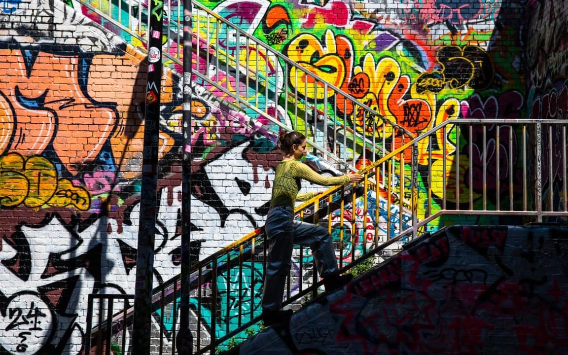 A woman climbs stairs beside a brick wall covered in colourful graffiti.