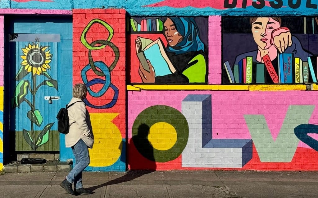 A person walks past a colourful mural featuring two women reading books.