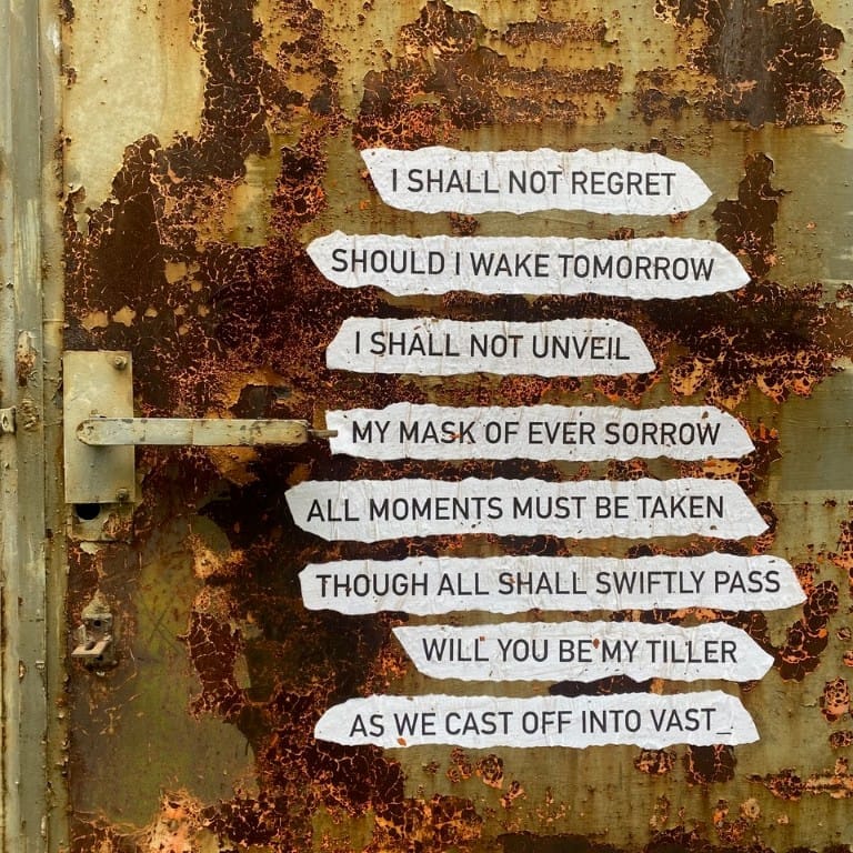 Torn paper strips printed with poem lines pasted onto a rust-covered metal surface.