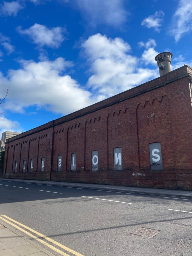 The word "Illusions" stencilled across boarded windows on a red brick building.