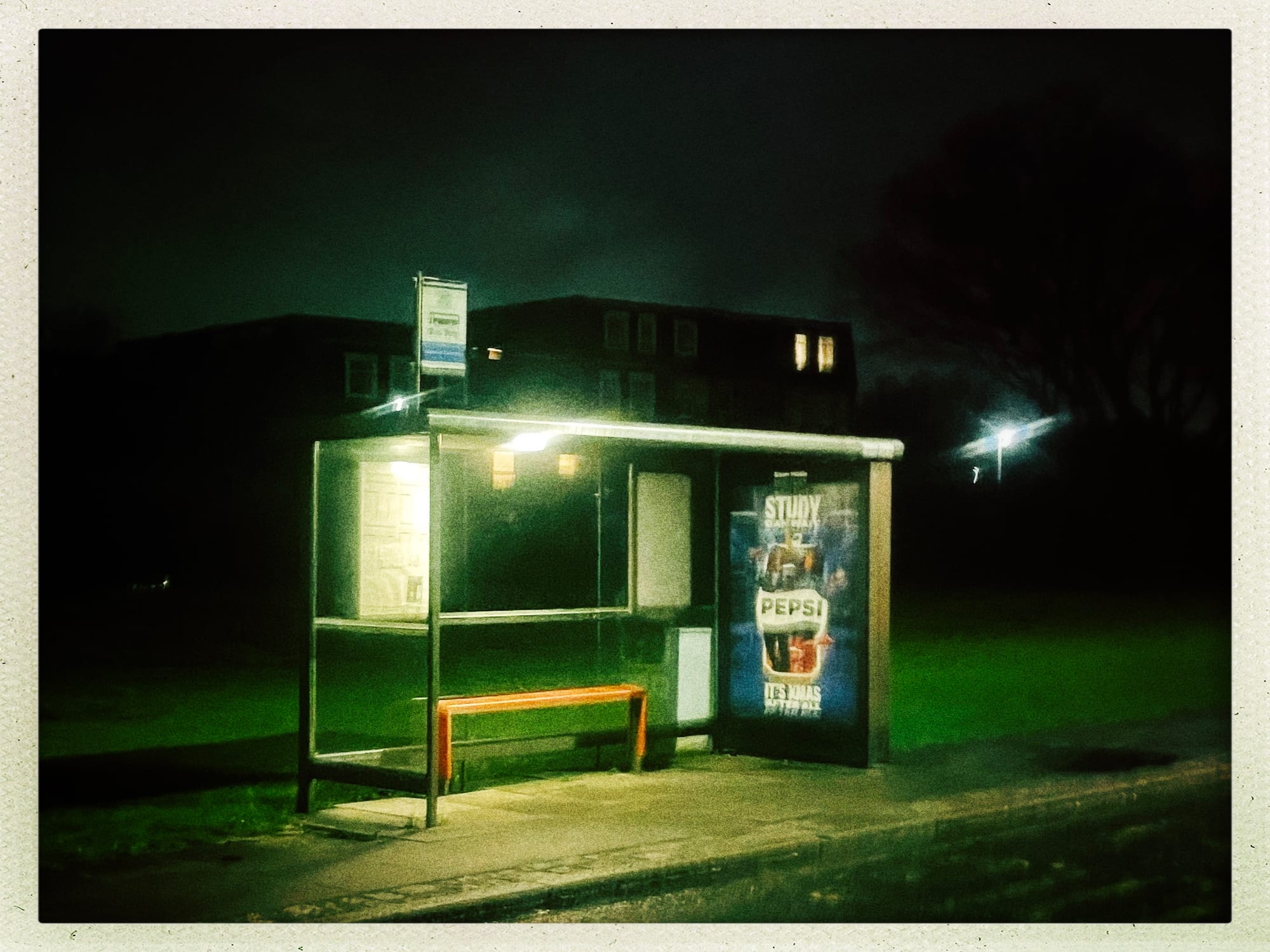 An empty bus shelter lit from inside at night, a Pepsi advert on the side panel.