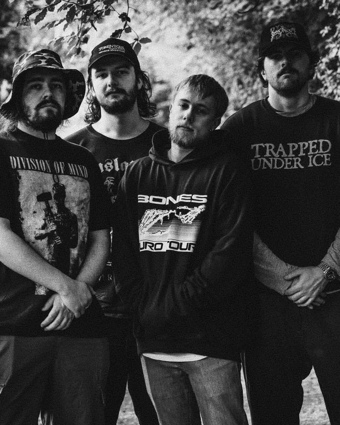Four-piece metal band Bitterwood pose outdoors in black band tees, black and white photo.