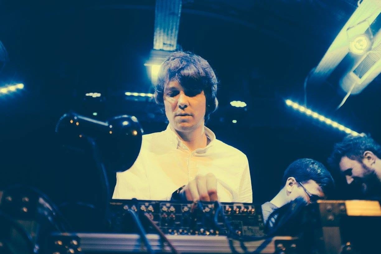 Steven Milne at the decks, lit blue, with two others beside him